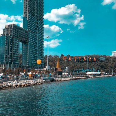 נוף פנורמי של העיר פטאיה – קו רקיע עירוני מודרני, בניינים רבי קומות, חוף ים חולף ומזח עץ קטן, בשעות היום עם שמיים בהירים ואור טבעי